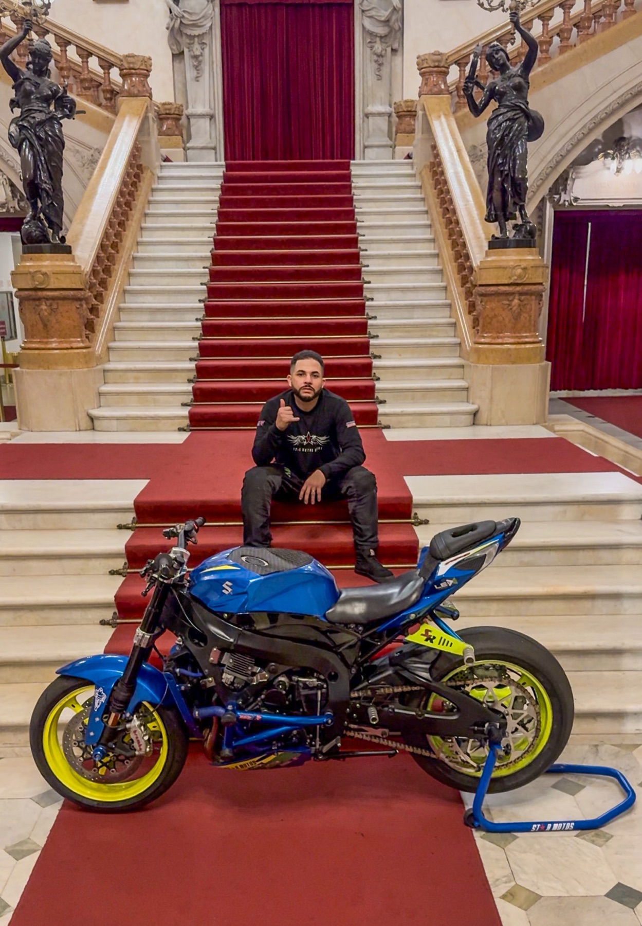 Darlan Rocha sentado na escadaria do Theatro Municipal ao lado da sua moto